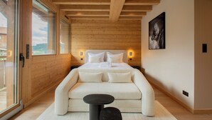 Ein Schlafzimmer mit Holzbalkendecke, einem Bett mit weißer Bettwäsche, einer Couch, einem kleinen Tisch und einem Bild an der Wand.