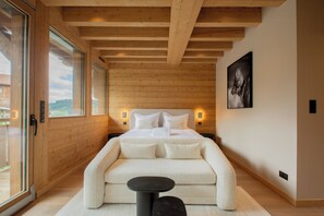 A bedroom with a wooden ceiling, a bed with white bedding, a sofa, a small table, and a painting on the wall. - Chalet with spa near ski slopes in La Mauselaine (Gérardmer)