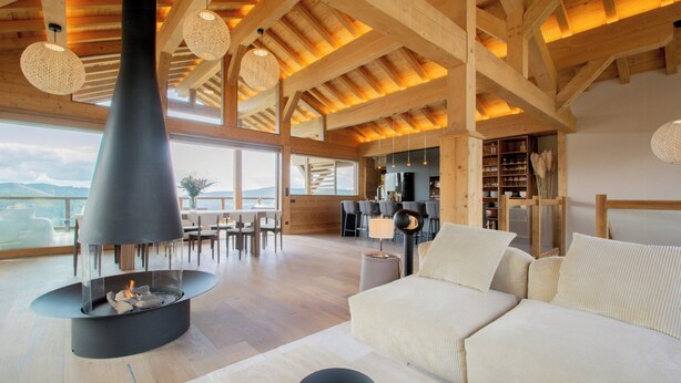 Ein großzügiger Wohnbereich mit Kamin, Holzbalken, einer Couch und einem Essbereich mit Tageslicht.