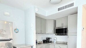 A compact kitchen with white cabinets, a microwave, and a refrigerator. - Bright Beachfront Studio + Pool (Myrtle Beach)