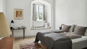 Un dormitorio con cama, una ventana con cortinas, un radiador, una lámpara y un cuadro en la pared.