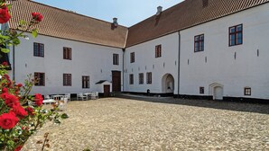Un patio con suelo de adoquines, edificios blancos con múltiples ventanas y una puerta central.