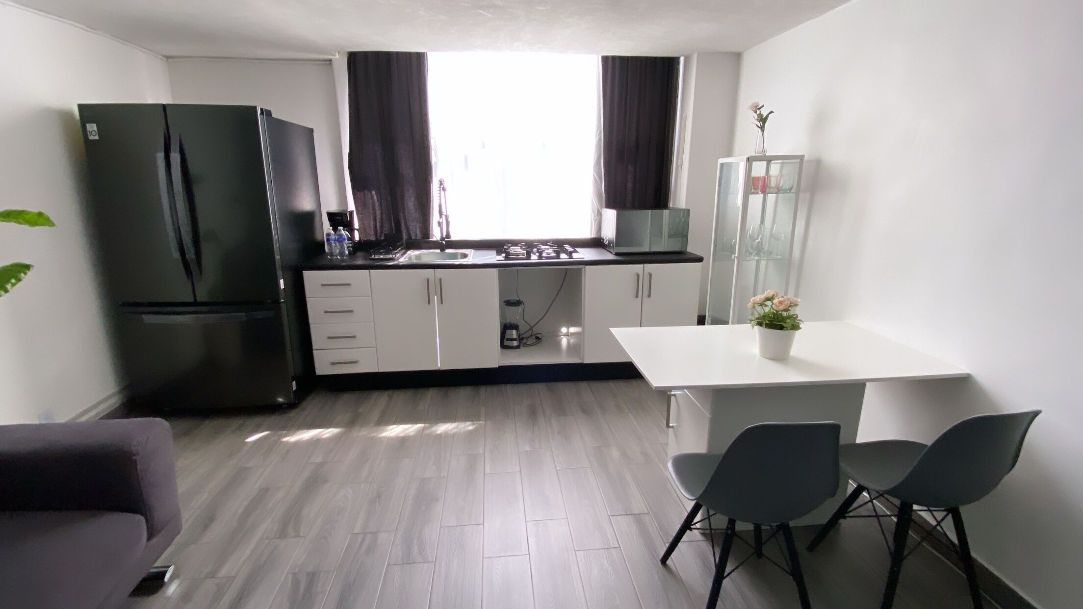 Een compacte keuken met een koelkast, kookplaat en spoelbak, een eettafel met stoelen en een kast met glazen deuren.