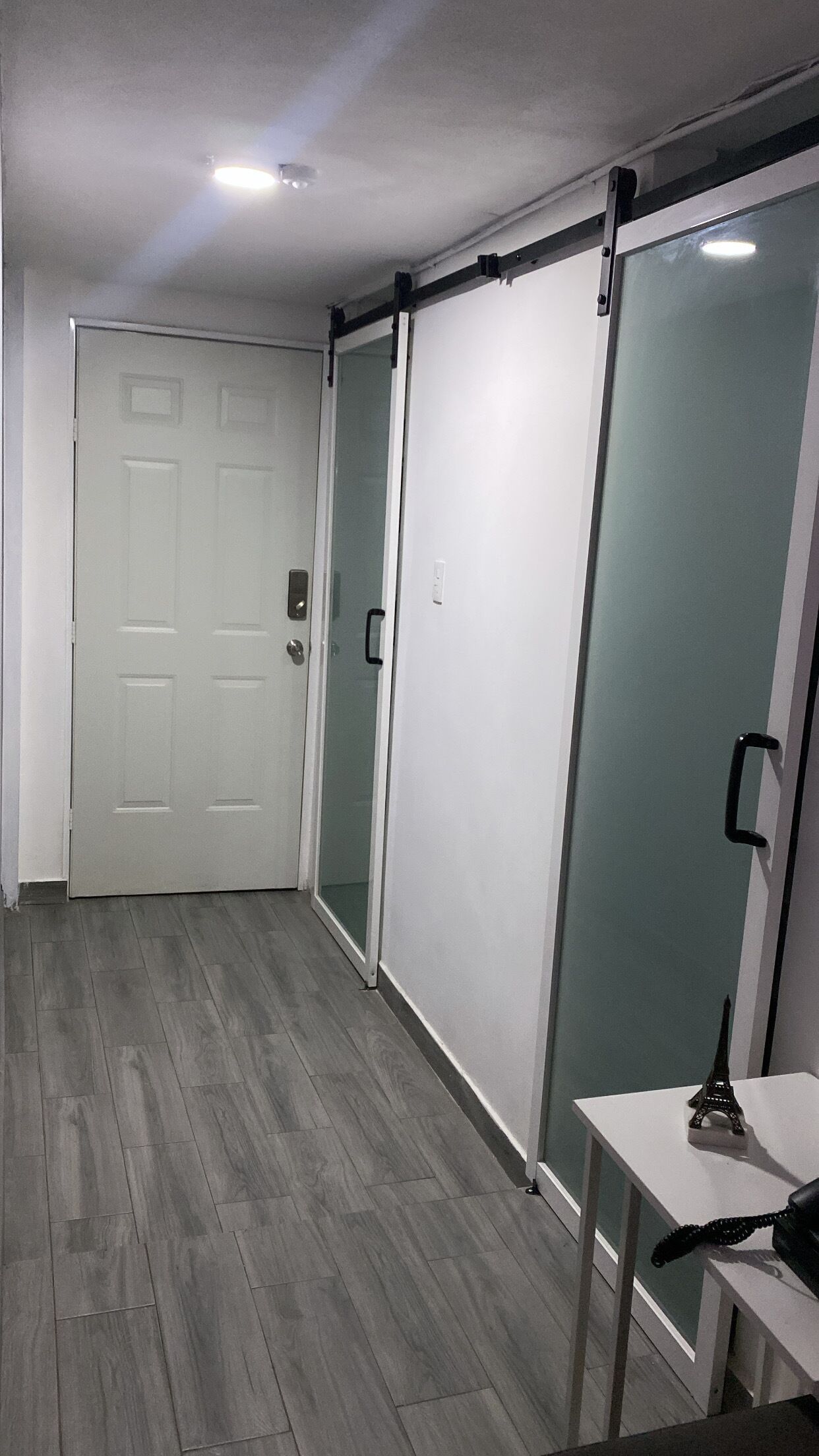 A hallway with a sliding door, a door with a handle, and a small table with a lamp.