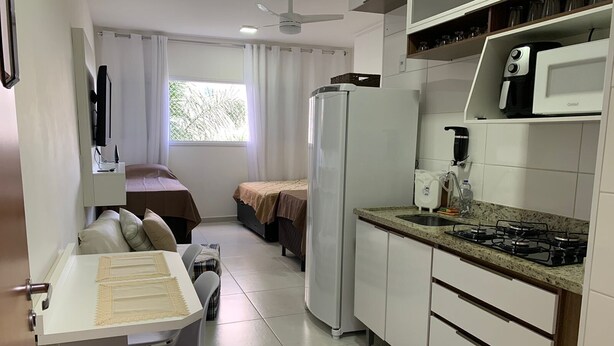 A compact kitchen with a refrigerator, microwave, and stove. There is a dining area with a table and chairs. - Oceana Suites Cachoeira Paulista (Cachoeira Paulista)