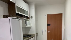A compact kitchen with a refrigerator, microwave, and stove, a small dining table with a chair, and a wooden door. - Oceana Suites Cachoeira Paulista (Cachoeira Paulista)