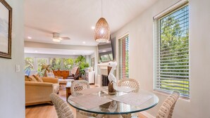 A modern living room with a glass table, wicker chairs, a ceiling fan, and a large window with blinds. - The Flamingo House - Sarasota (Sarasota)