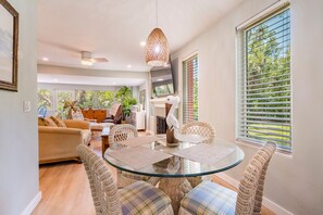 Ein modernes Wohnzimmer mit Glastisch, Korbstühlen, Deckenventilator und großem Fenster mit Jalousien.