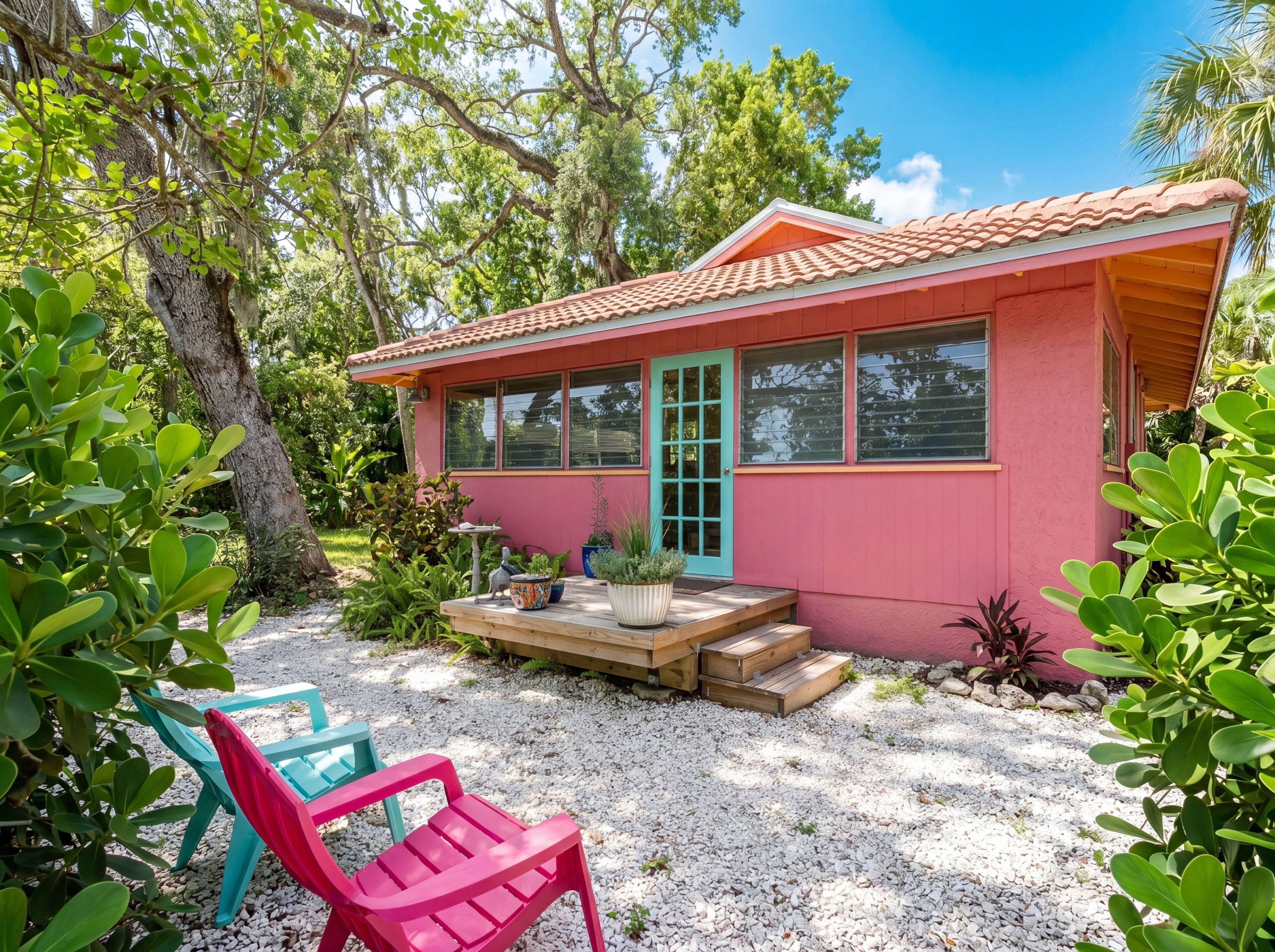 A pink house with a tiled roof, a front porch, and a gravel driveway.