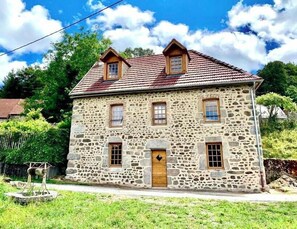 A two-story stone building with a red-tiled roof, a wooden door, and multiple windows. - Traditional house in Millevaches (Croze)