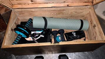 Une boîte en bois contenant du matériel de fitness, notamment des haltères, un tapis de yoga, des bandes de résistance et une bouteille d’eau.