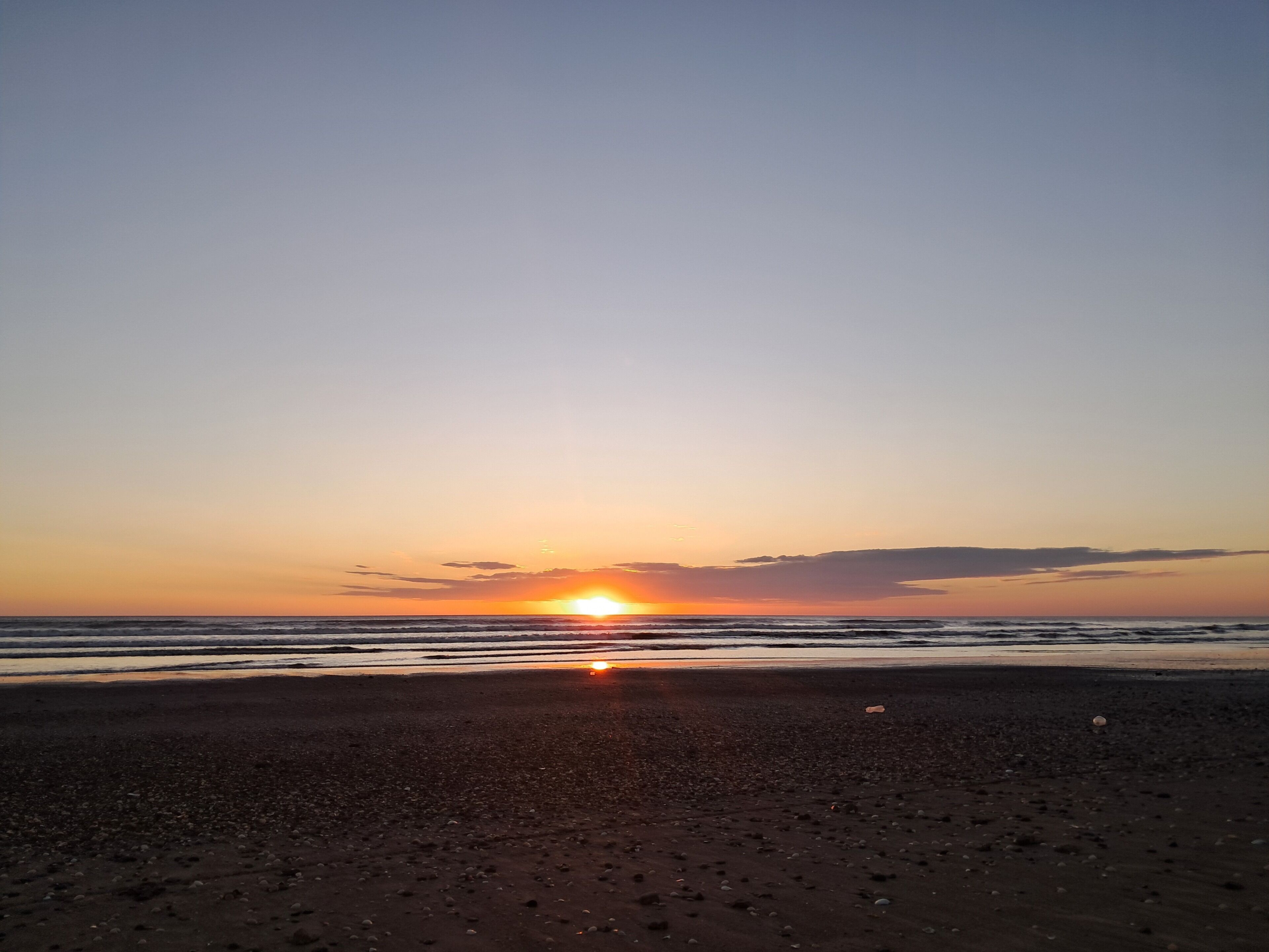 Una playa al atardecer, con el sol poniéndose en el horizonte.