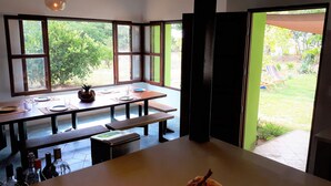 Un coin repas avec une table dressée pour deux personnes, un banc et une vue sur le jardin grâce à de grandes fenêtres.