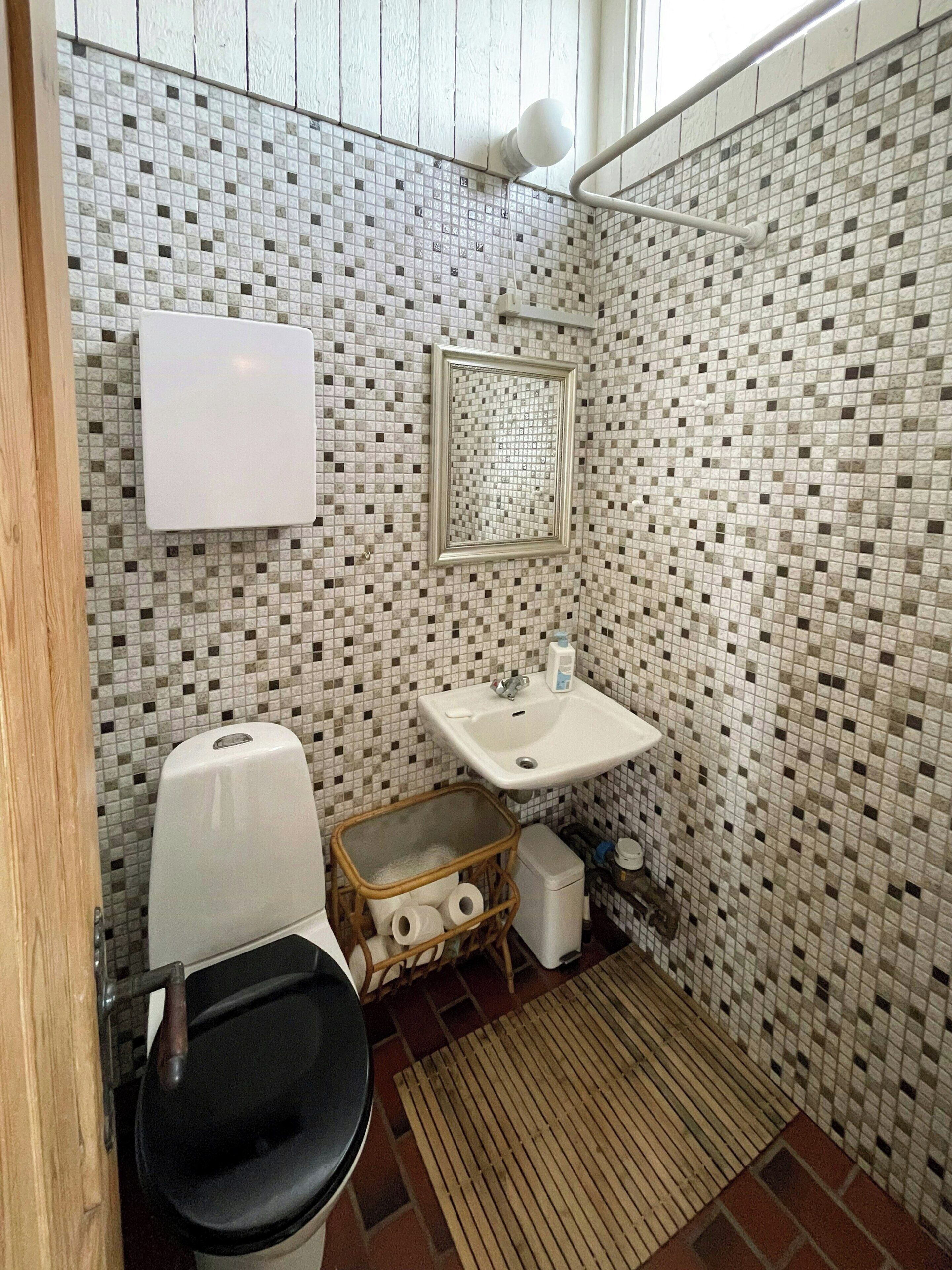 Ein Badezimmer mit einer mosaikverkleideten Wand, einem weißen Waschbecken, einem Spiegel und einer Toilette.