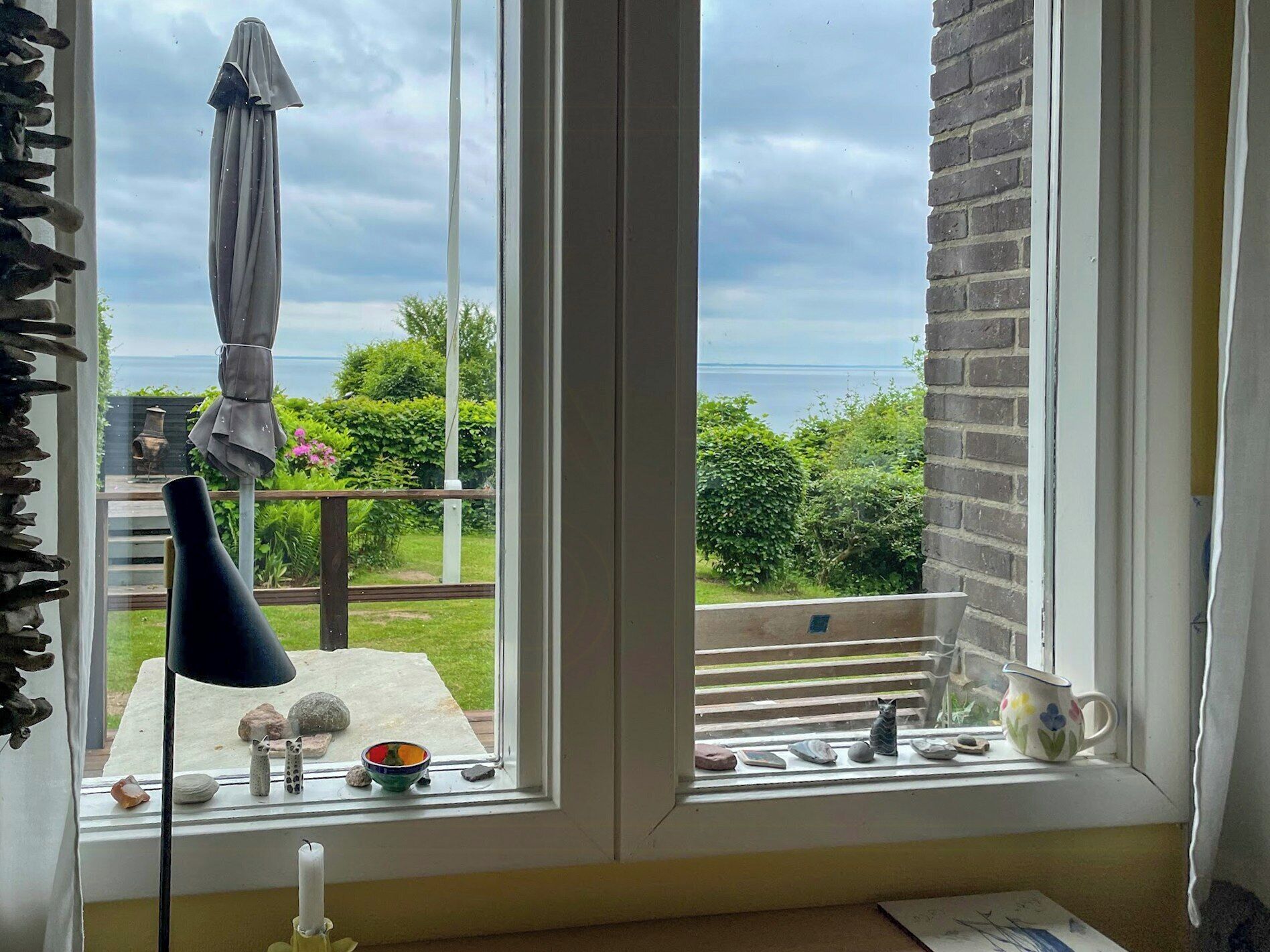 A room with a large window overlooking a garden and a body of water.