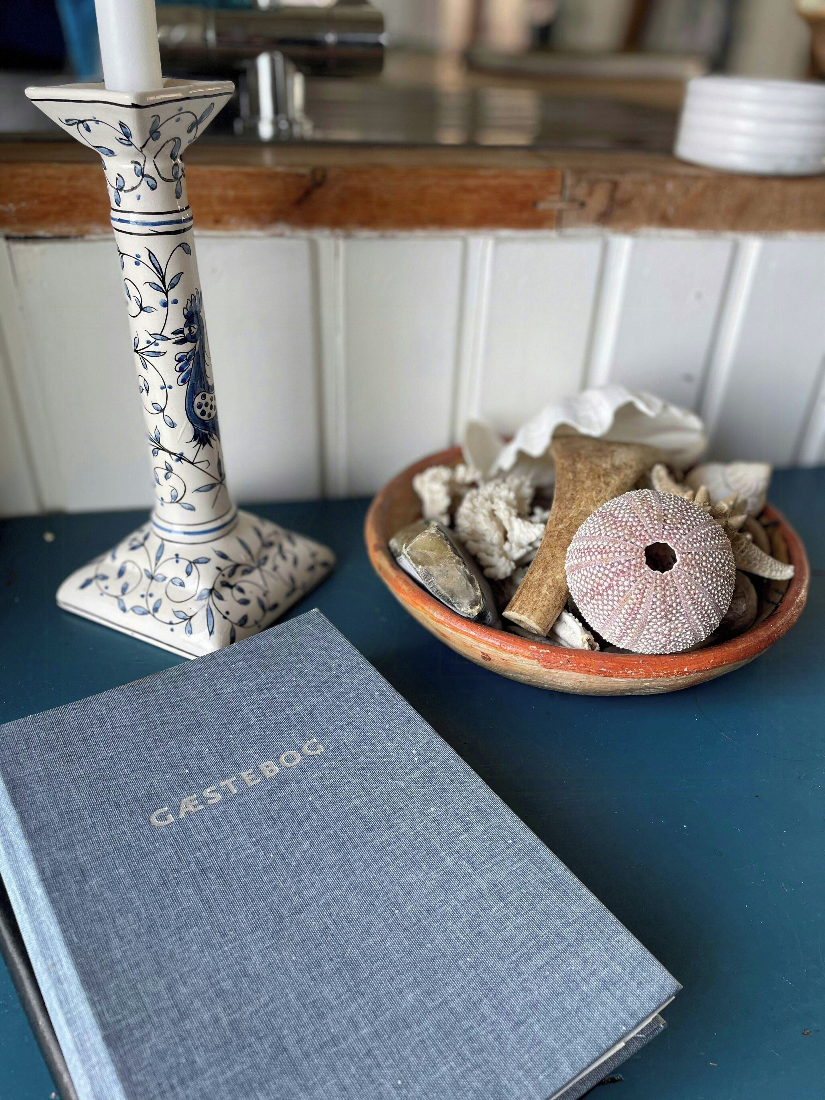Un libro azul, un jarrón decorativo y un cuenco con caracoles sobre una mesa.