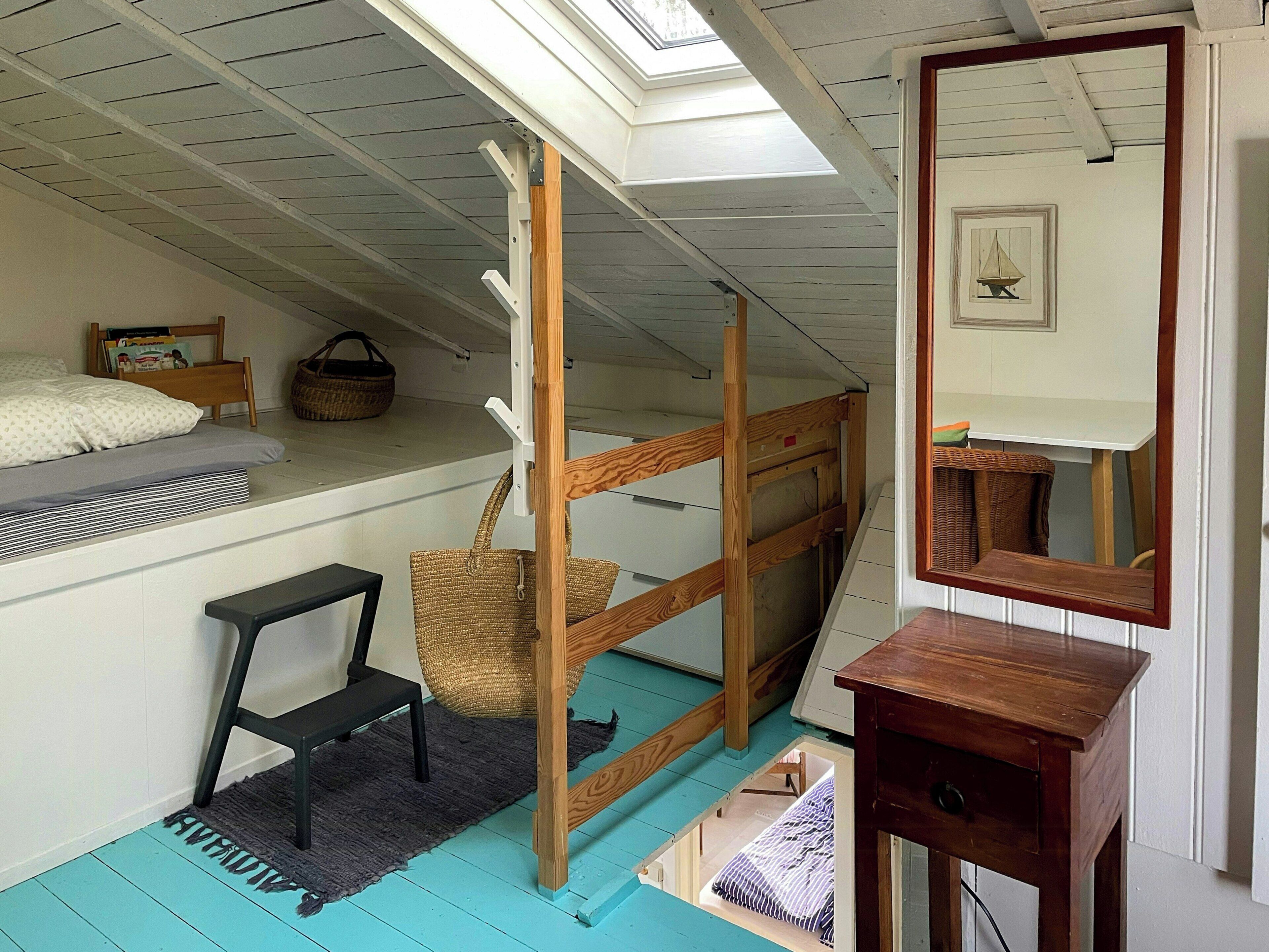 Un dormitorio tipo loft con una cama litera, un escritorio pequeño, un espejo y un tragaluz.