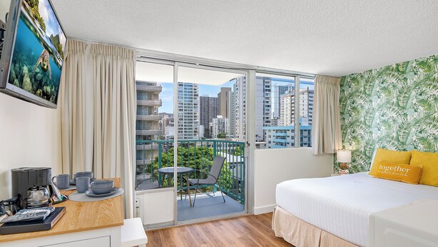 Une chambre d’hôtel avec un balcon, un lit, un bureau avec un ordinateur et une télévision.