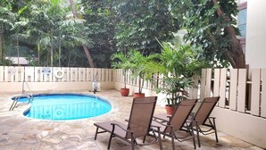 Une piscine dont le fond est recouvert de pierres, entourée de plantes en pot et de mobilier d’extérieur.