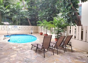 Ein Schwimmbecken mit Steinböden, umgeben von Topfpflanzen und Gartenmöbeln.