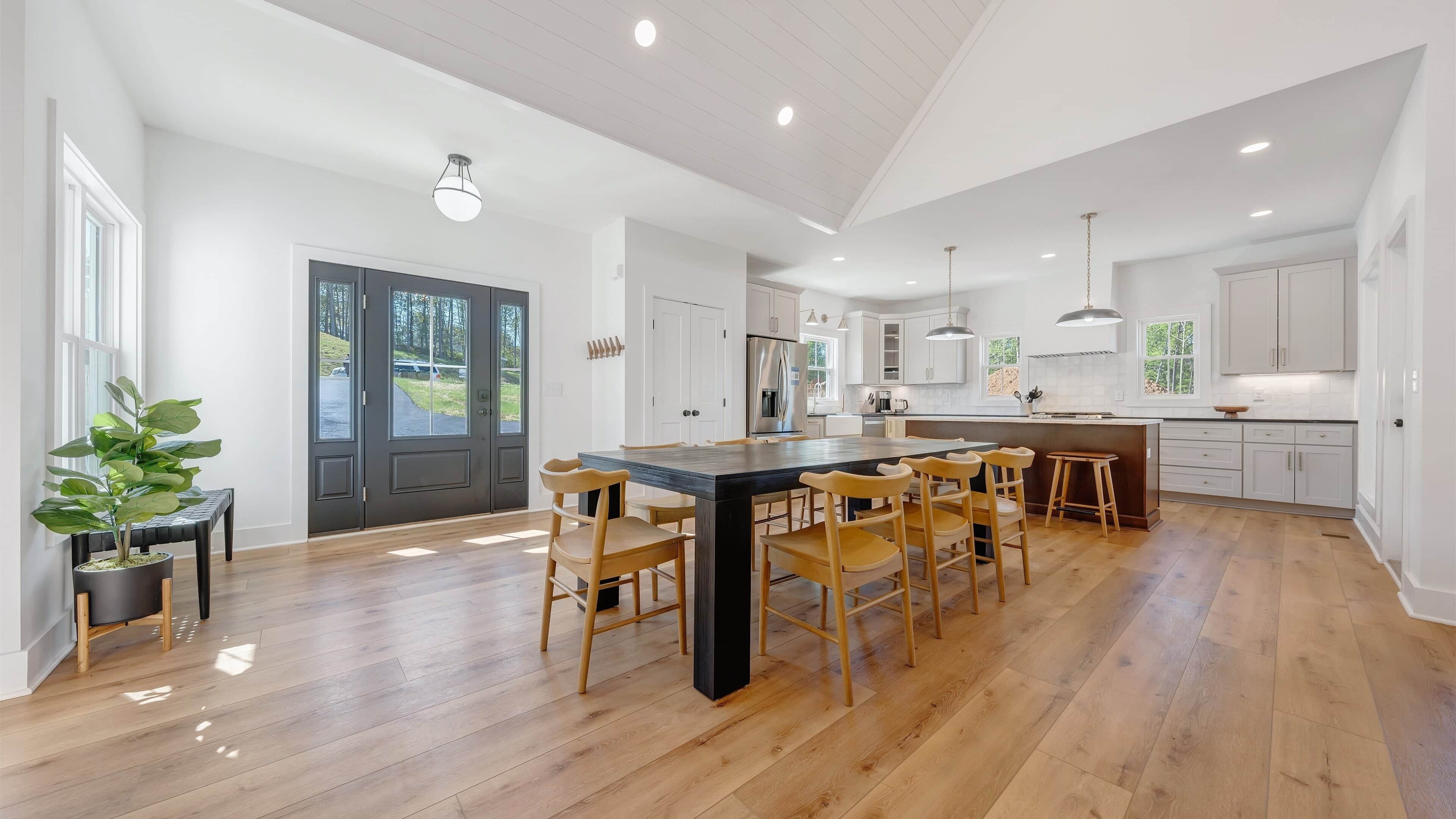 A spacious kitchen with a central island, wooden chairs, and a large window.