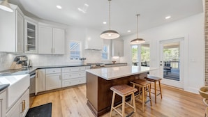 A modern kitchen with white cabinetry, a central island with stools, and a view to an outdoor deck. - Watermark Bluff (Bedford County)