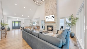 A spacious living area with a fireplace, a large sofa, and a dining area with a kitchen in the background.