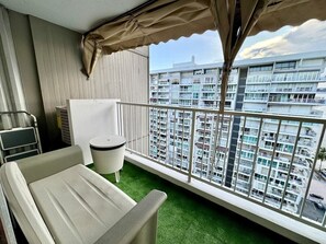 Ein Balkon mit Blick auf ein Hochhaus, einem Tisch, einem Mülleimer und einem Stuhl.