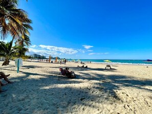 A beach with palm trees, umbrellas, and people relaxing. - Charming Isla Verde with Pool & Beach Access (Carolina)