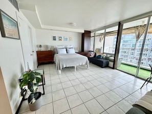 Ein Schlafzimmer mit einem Bett, einem Sofa, einem Esstisch und einem großen Fenster mit Blick auf Gebäude.
