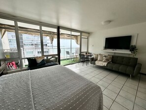 A hotel room with a bed, a sofa, a TV, and a balcony with a view of buildings. - Charming Isla Verde with Pool & Beach Access (Carolina)