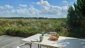 Et bord dækket udendørs med stole, en kurv, tallerkener og kopper.