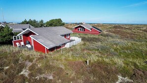 En rød bygning med fladt tag, hvide ydervægge og en lille veranda med stole.