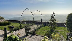 A garden with a stone wall, a bench, and a view of distant hills.