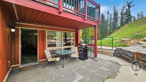 Un edificio de dos pisos con un patio que cuenta con una mesa, sillas, una parrilla y vistas a un paisaje montañoso.