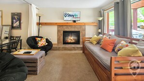 Una sala de estar con chimenea, un sofá, una silla, un televisor y un cartel que dice 'StayIn'.