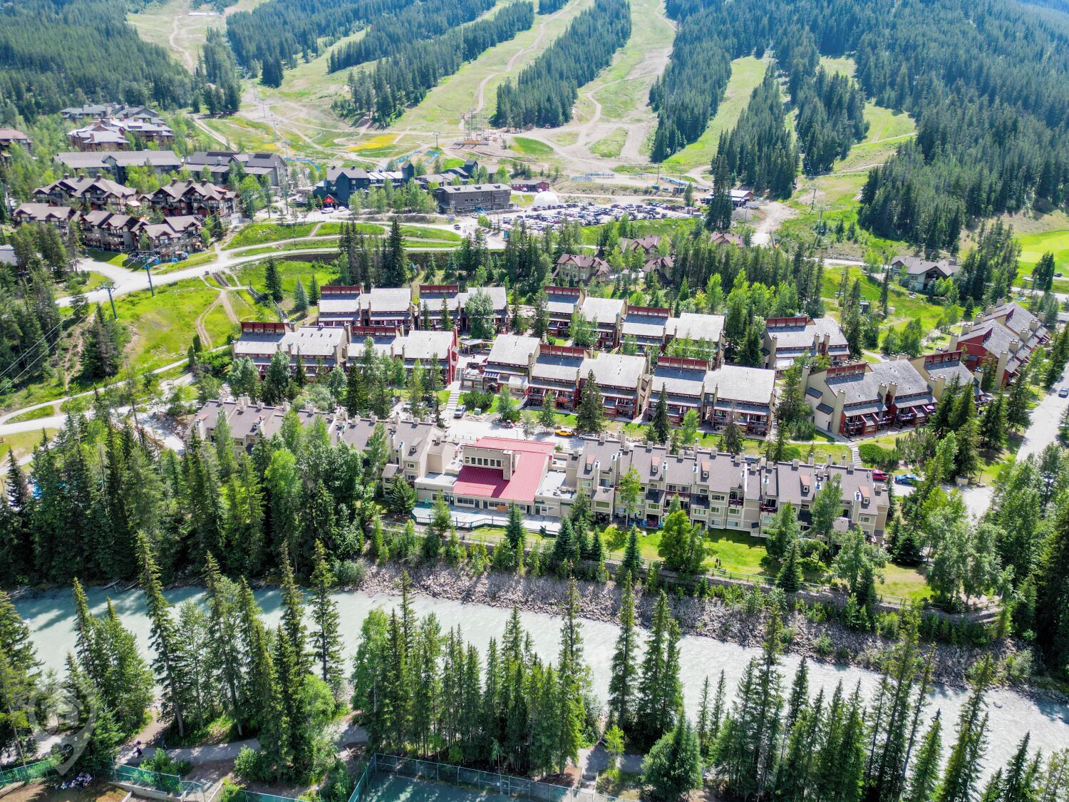 An aerial view of a resort with multiple buildings, a river, and surrounding forest.