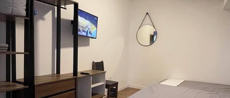 A bedroom with a bunk bed, a desk, a chair, a TV, a mirror, and a bed.