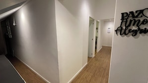 A hallway with white walls and wooden flooring, leading to a room with a door. - Downtown Florianópolis, everything nearby, comfortable, fully equipped, 4 bedrooms with AC and 2 bathrooms. (Florianópolis)