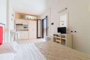 Una habitación de hotel con cama, escritorio, televisor, kitchenette y baño.