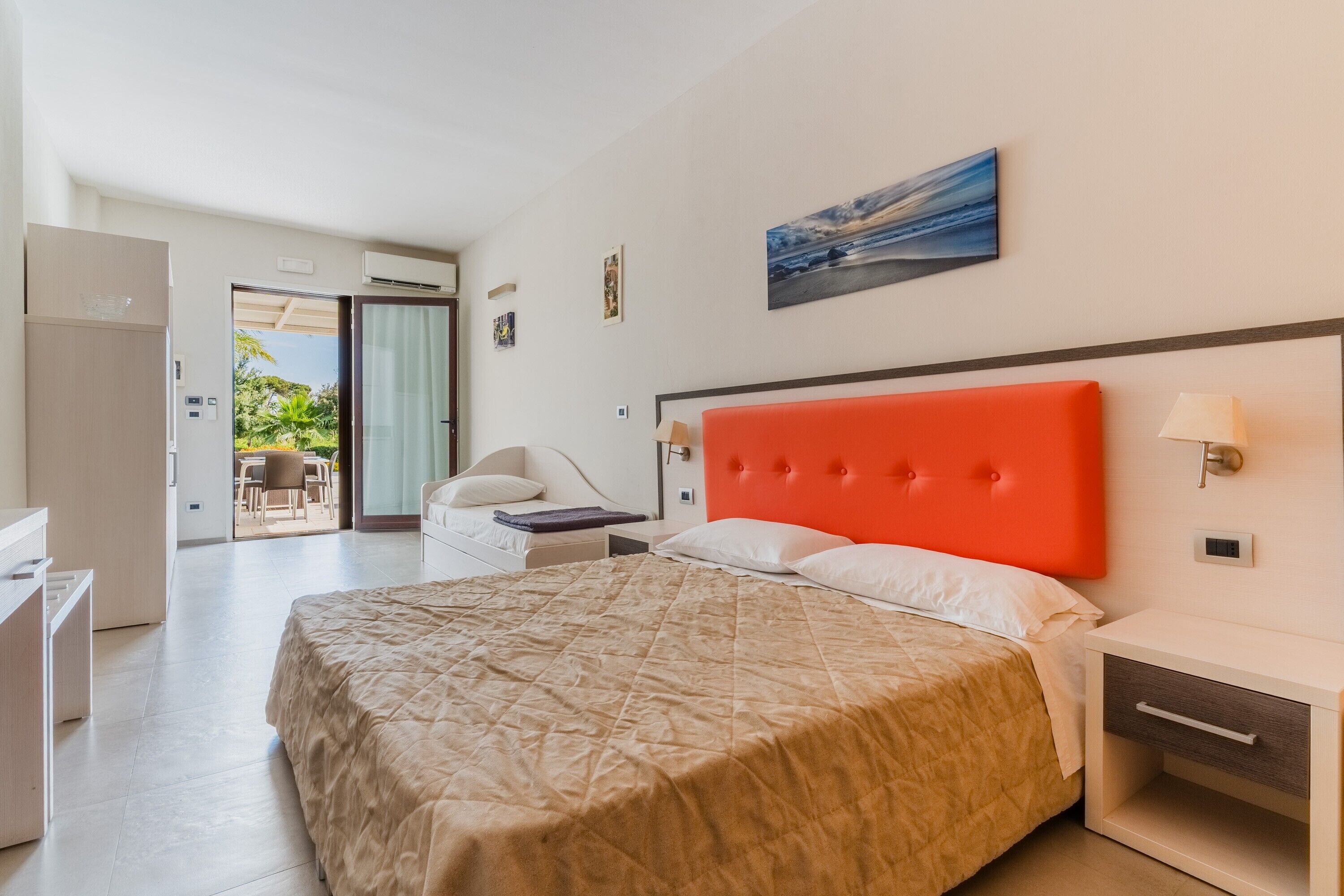 Habitación de hotel con cama, escritorio, silla, ventana y puerta que da a un balcón.