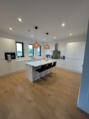 A modern kitchen with a central island, pendant lighting, and a view of greenery outside.