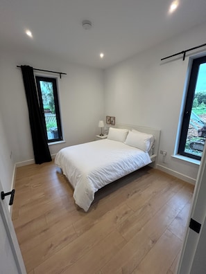 A bedroom with a bed, a window, a bedside table, and a door. - Modern Rural Ireland Retreat – Spacious & Peaceful Countryside Escape. (Derryadd)