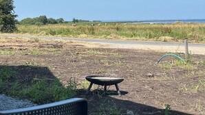 Un'area sterrata con un tavolo e una panchina in metallo, un prato con delle mucche e un cielo sereno.