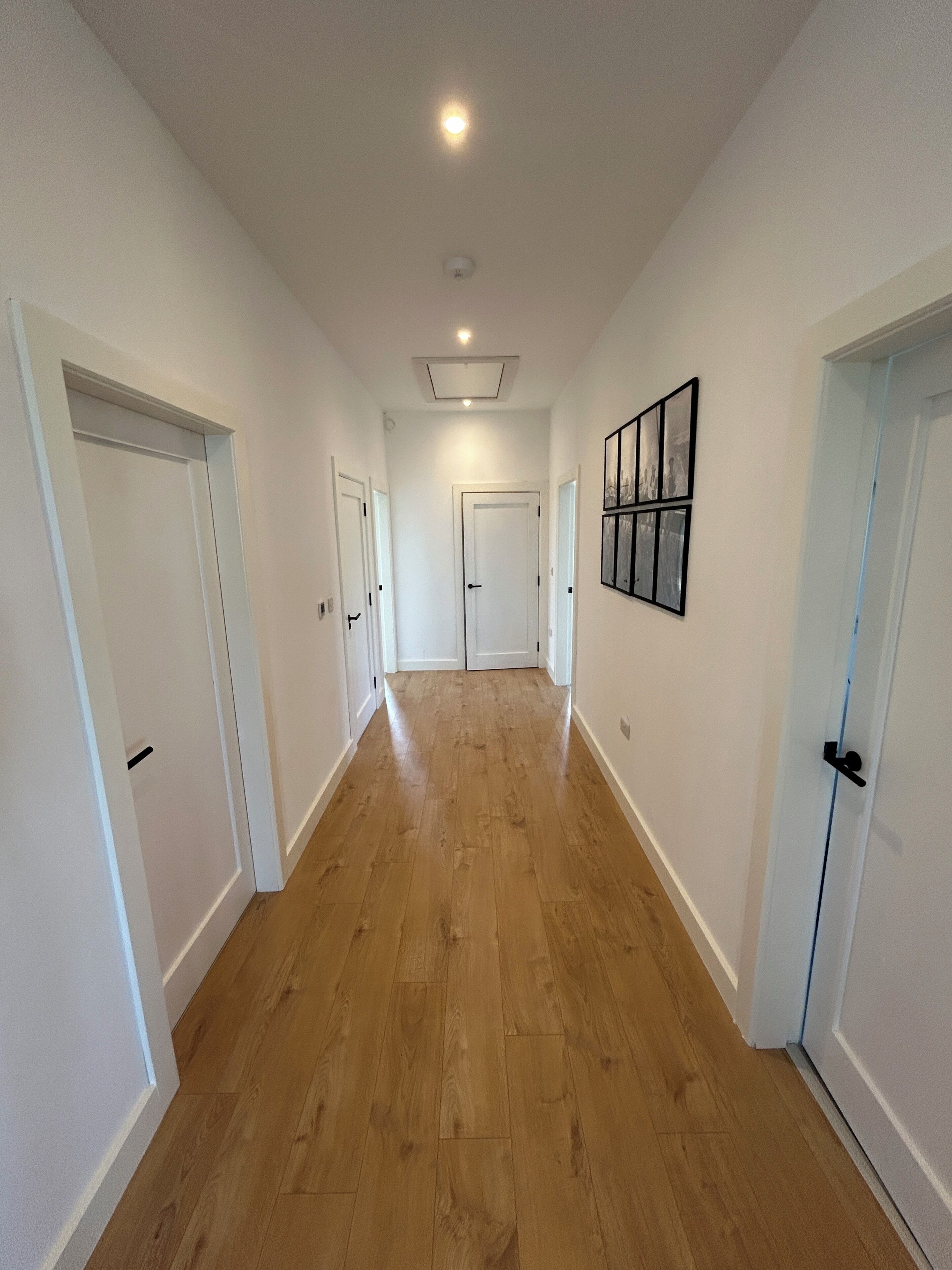 A hallway with wooden flooring, white walls, and doors leading to rooms.
