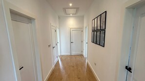 Un corridoio con pavimento in legno, pareti bianche e porte che conducono a delle stanze.