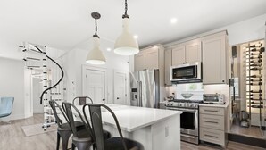 A modern kitchen with a central island, stainless steel appliances, and pendant lighting. - Designer Home with Wraparound Porches & Fire Pit (Bourne)