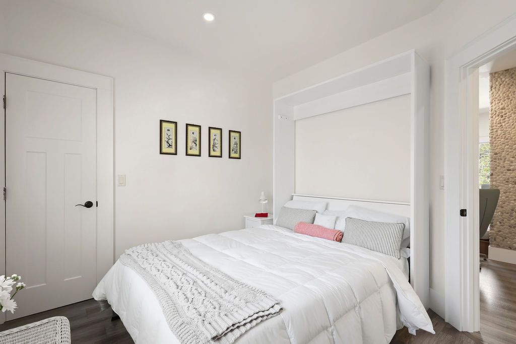 A bedroom with a bed, a nightstand, a door, and a wall with framed pictures.