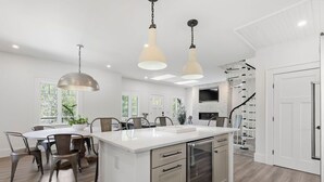 A modern kitchen with a central island, pendant lights, a built-in oven, and a staircase leading to a loft area. - Designer Home with Wraparound Porches & Fire Pit (Bourne)