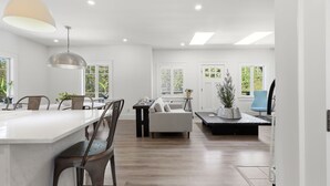 A modern interior with a kitchen island, dining area, and seating space. - Designer Home with Wraparound Porches & Fire Pit (Bourne)